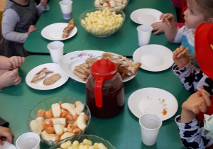 Grupa dzieci siedzi przy stole i je owocowy poczęstunek.